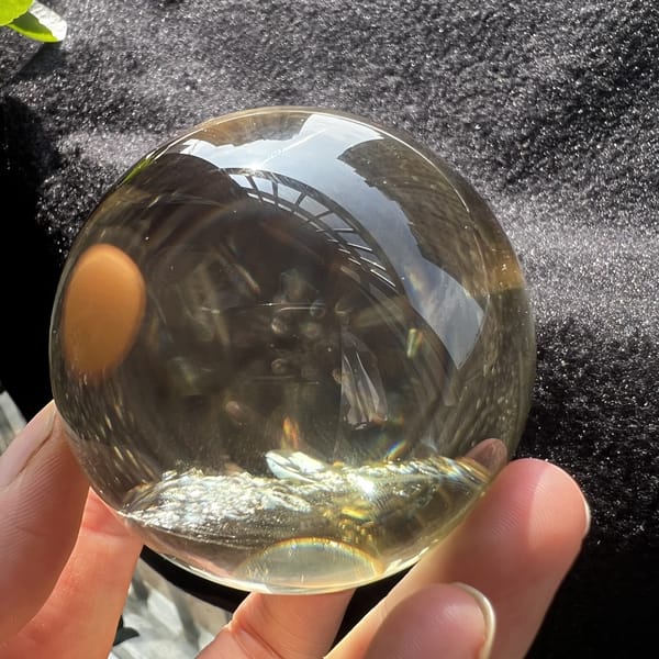 Citrine sphere on grey cloth reflecting a hand, inclusions at the base
