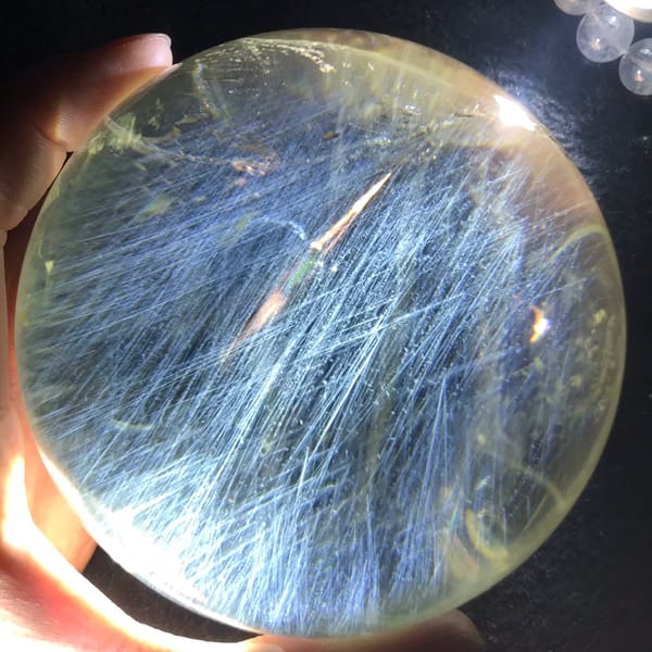Pale citrine sphere filled with silky blue needles under a bright light