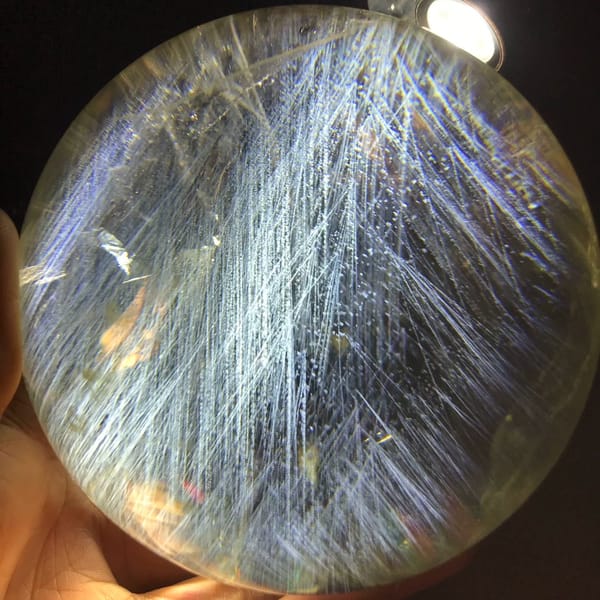 Dense sprays of blue needles crossing the full face of the citrine sphere