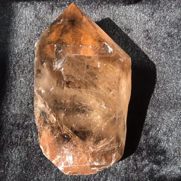Smoky citrine freeform point on black velvet, golden rutile sweeping through its body