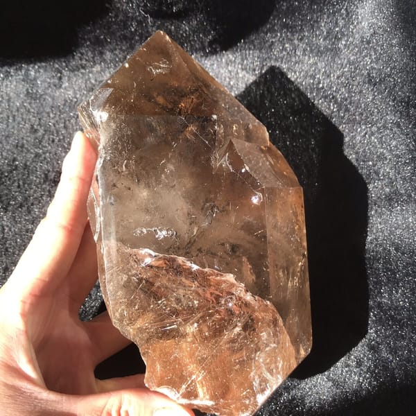 Hand supporting the freeform from the side, smoky body and rutile visible together