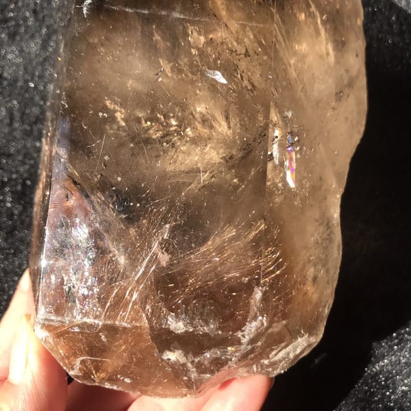 Close-up through a polished face showing golden rutile sprays and a small rainbow