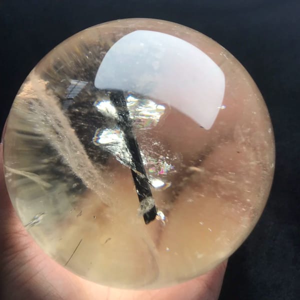 Pale citrine sphere on black with a black tourmaline needle and silvery flakes
