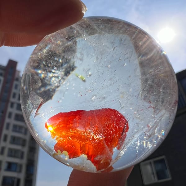 Clear quartz sphere held to the sky with a vivid red hematite inclusion glowing