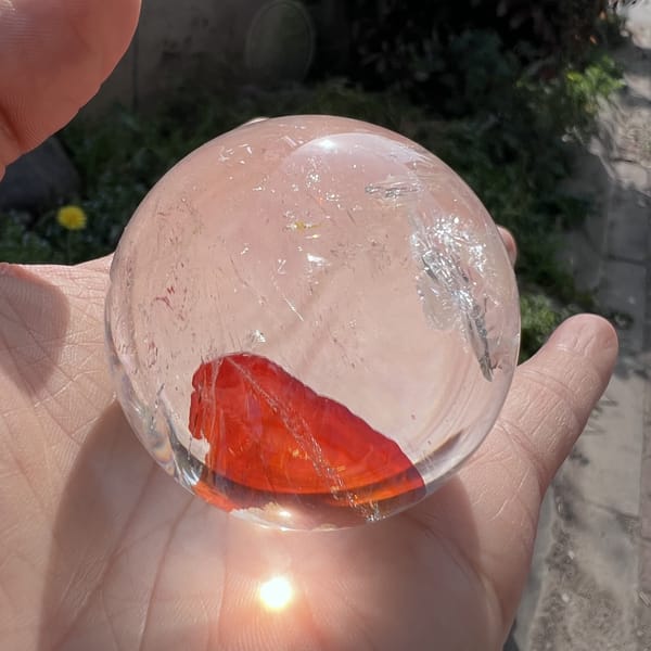 Red fire quartz sphere held in sunlight with a veil near the top edge