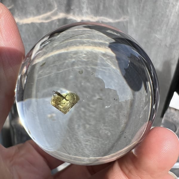 Heart inclusion seen through the clear sphere with a grey wall behind