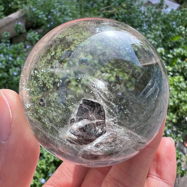 Clear quartz sphere in sunlight with a dark mica flower near its centre
