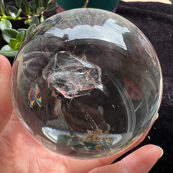 Large inner crystal with tan wisps beneath it, sphere held over plants