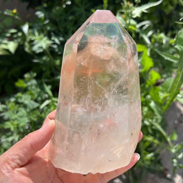 Red rabbit-hair quartz tower in hand, peach-red inclusions forming a mountain below the tip