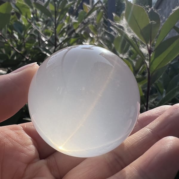 Sphere resting in palm in garden light, translucent milky body