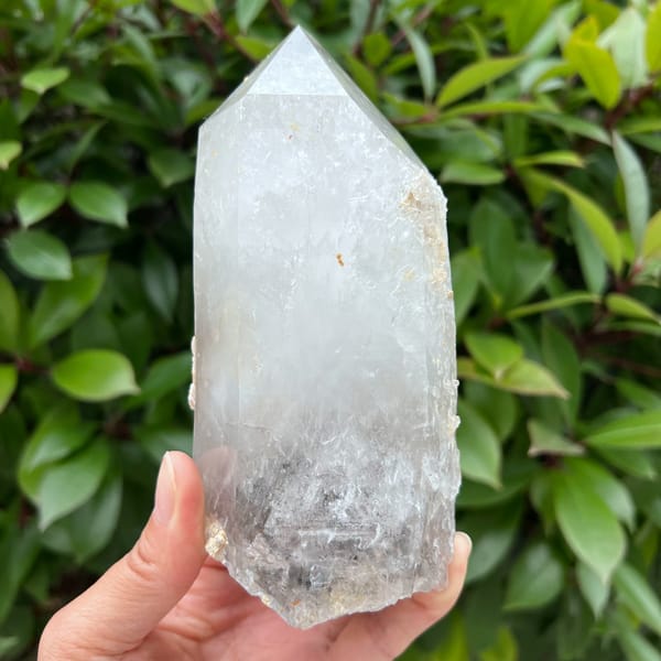 Clear quartz point held upright with a grey zone toward the base