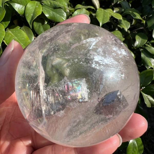 Clear quartz sphere in the hand with dark skeletal plates and a rainbow