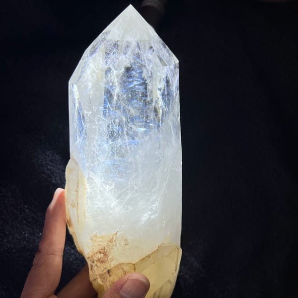 Large quartz point on black cloth with blue needle wisps glowing inside