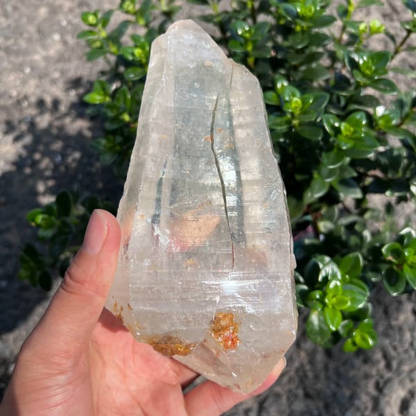 Clear quartz crystal with orange flecks at the base and a pink inclusion