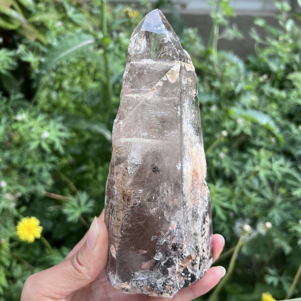 Clear quartz point with peach patches and dark specks near the base
