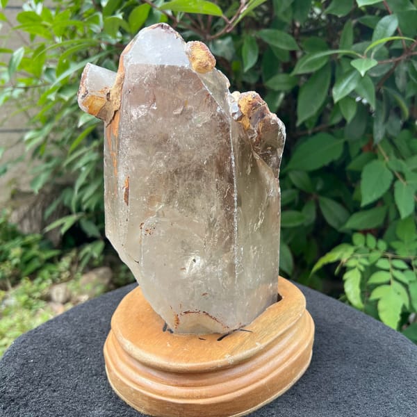 Large old-stock clear quartz standing on a light wooden stand outdoors