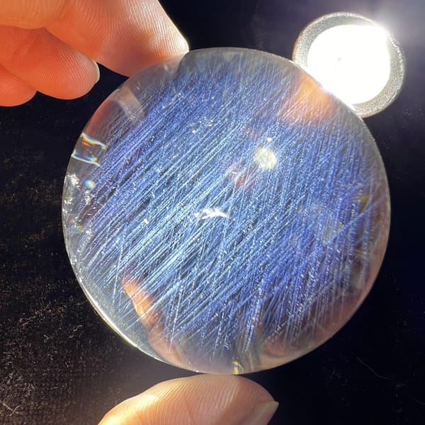Clear quartz sphere glowing blue under a torch with dense needle inclusions