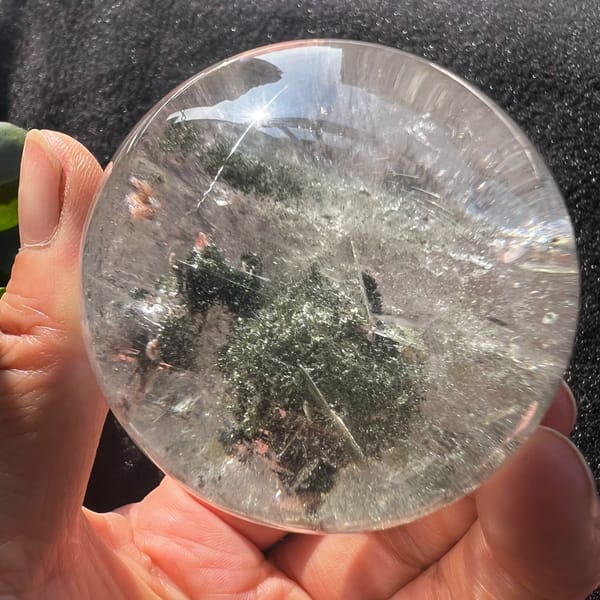 Green phantom quartz sphere with a dark mossy mound in the centre
