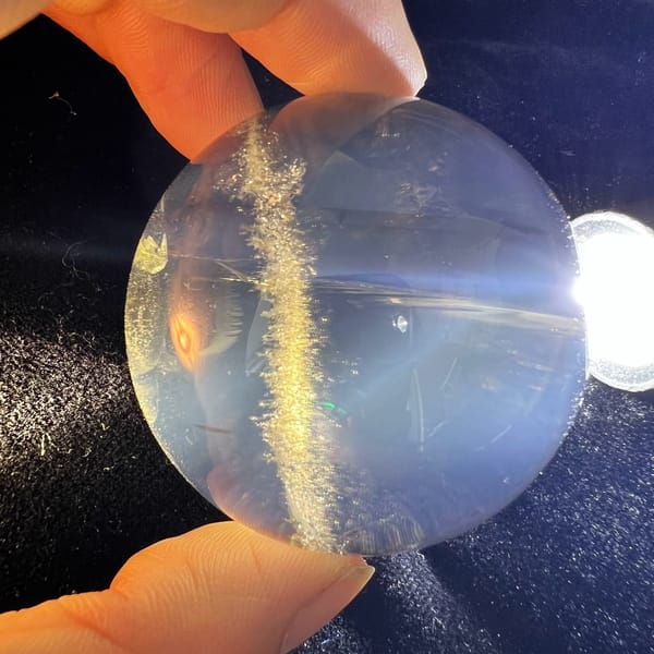 Smoky quartz sphere backlit by a torch showing a band of golden needles and blue haze
