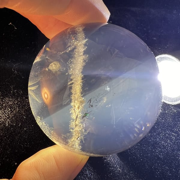 Smoky quartz sphere under torch with golden band and dark specks