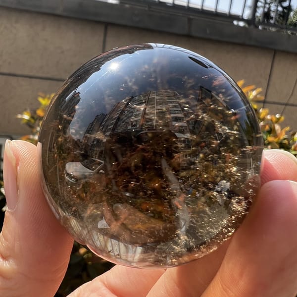Smoky quartz sphere in daylight with fine inclusions and reflections