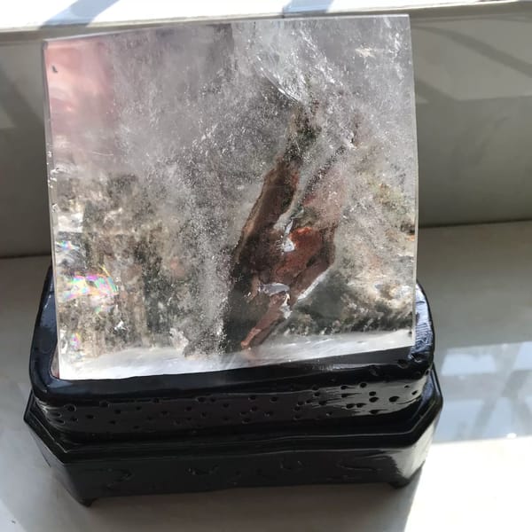 Polished quartz freeform on a dark carved stand with a red-brown phantom plume