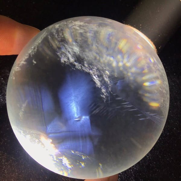 Rainbow arc along the upper edge above blue needle zones inside the sphere