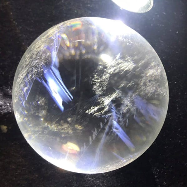 Sphere on dark glitter cloth showing fine blue needles and white flecks