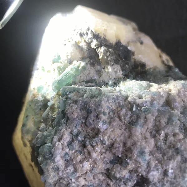 Torch-lit close view of green-blue tourmaline and lilac matrix