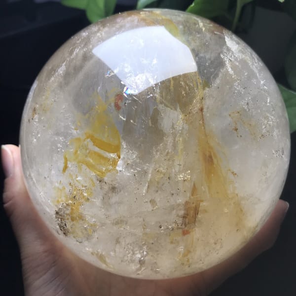 Clear quartz sphere showing a curving yellow streak and faint red fleck