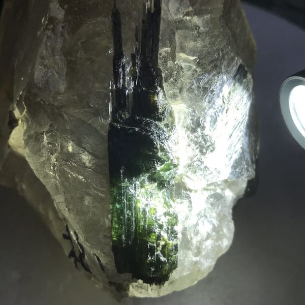 Bottle-green tourmaline glowing under backlight inside the quartz