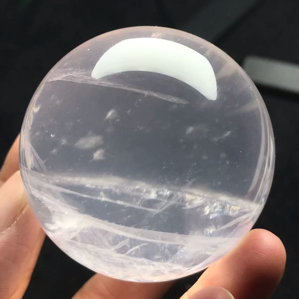 Transparent pink sphere in hand with fine white inclusions across the middle