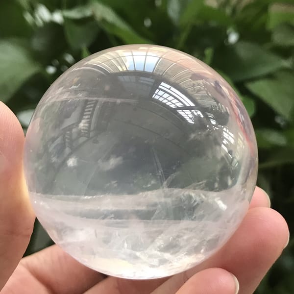 Rose quartz sphere held up to daylight, white band near the base