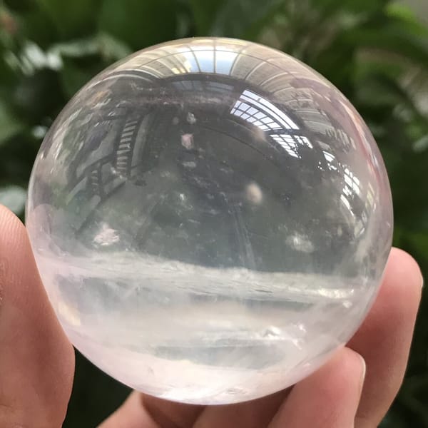 Icy sphere reflecting trees, faint pink tint throughout