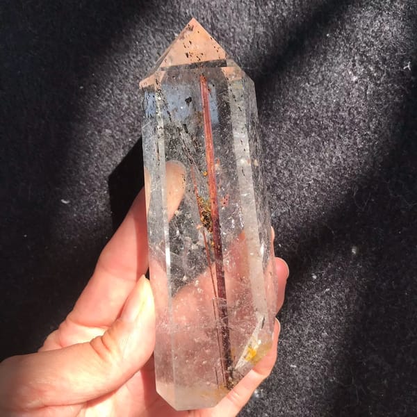 Polished quartz point in hand with a thick copper-red rutile rod inside