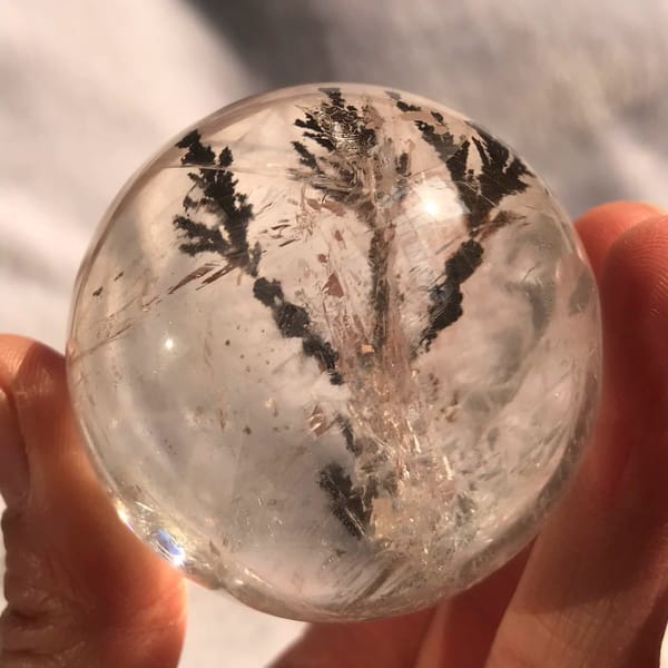 Small clear quartz sphere in hand with a dark branching tree inclusion