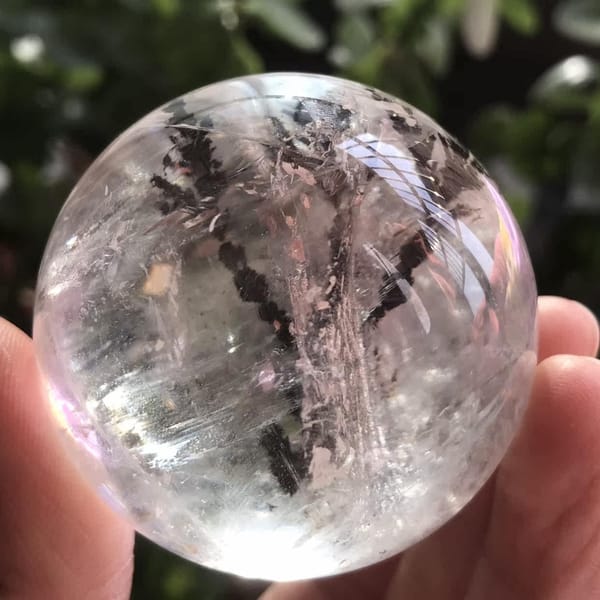 Quartz sphere photographed outdoors against green leaves, tree inclusion visible