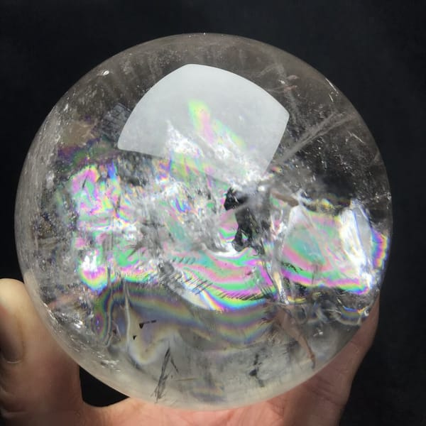 Bright rainbows and dark specks inside the clear quartz ball