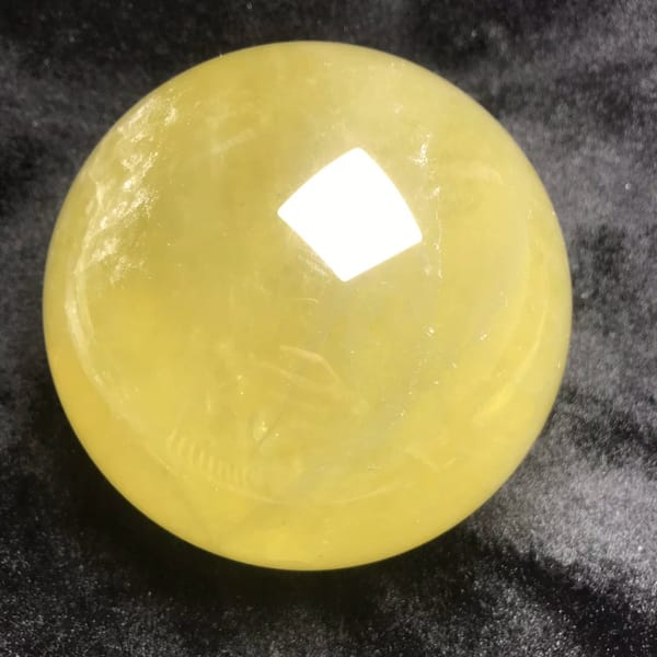 Large bright yellow citrine sphere resting on dark velvet