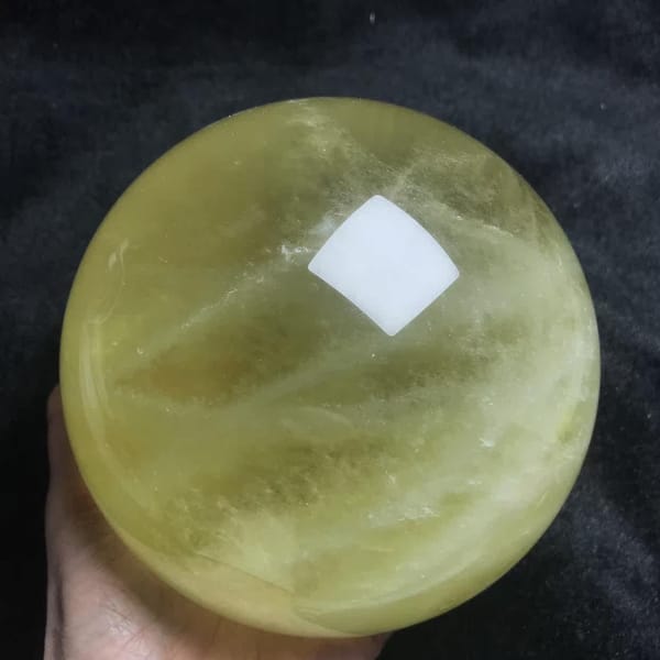 Large citrine sphere supported by hand with soft yellow bands