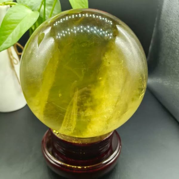 Large citrine sphere on a dark wooden stand beside a green plant