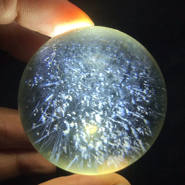 Backlit citrine sphere held between fingers, packed with blue needles