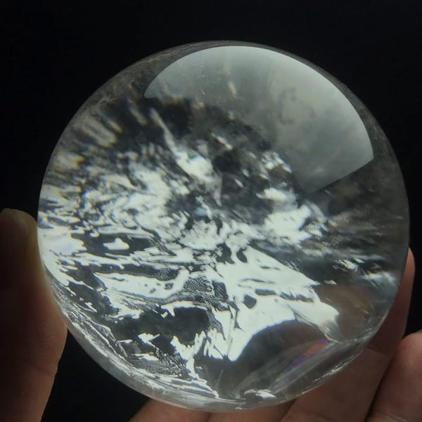 Brazilian quartz sphere filled with jagged white inclusion clouds held against black