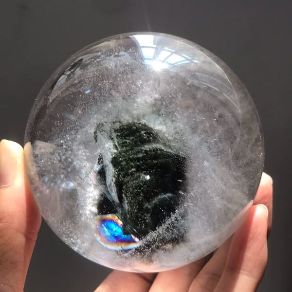 Brazilian quartz sphere with a dark green layered phantom and a blue rainbow below