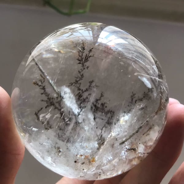 Clear garden quartz sphere with dark branching tree-like inclusions above a white cloud