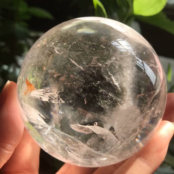 Brazilian enhydro quartz sphere in hand with white veils and an orange-brown feather