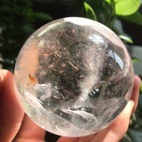 Orange-brown feather inclusion at the left of the clear quartz sphere