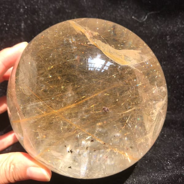 Large rutilated quartz sphere held in hand, packed with golden rutile needles