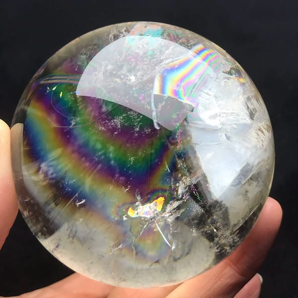 Brazilian quartz sphere with a wide rainbow arc and white clouds at right