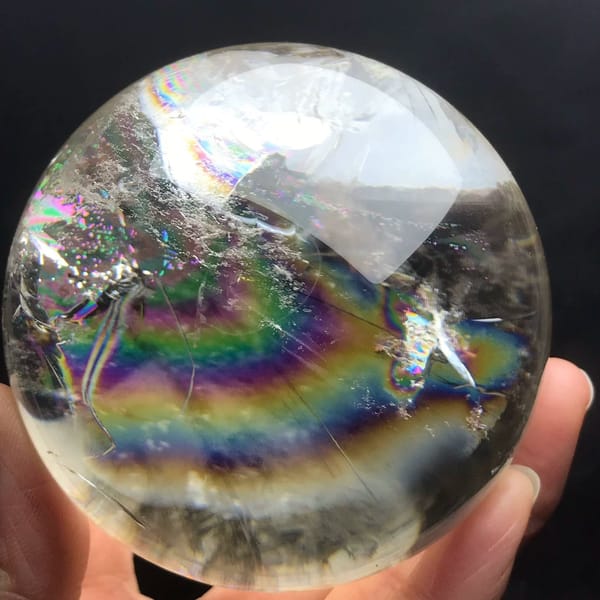 Rainbow band sweeping beneath white inclusion clouds in faintly yellow quartz